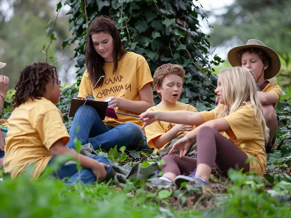 Early childhood educator facilitating outdoor learning, observing and guiding children in a natural setting